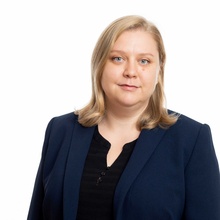 Porträt einer Frau mit blonden Haaren in einem blauen Blazer vor weißem Hintergrund.