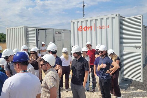 Gruppe von Menschen mit Helmen vor Containern auf einer Baustelle.
