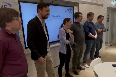 Sechs Personen stehen nebeneinander vor einer Präsentationsleinwand.