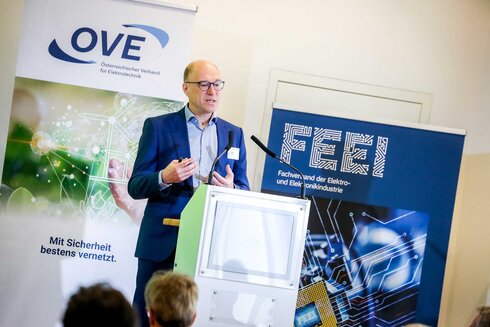 Mann hält Vortrag vor Publikum, mit OVE- und FEEI-Logos im Hintergrund.