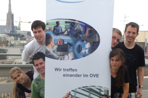 Sechs Personen posieren fröhlich vor einem OVE-Banner in urbaner Umgebung.