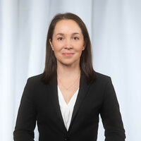 Portrait einer Frau in schwarzem Anzug vor einem hellen Hintergrund.