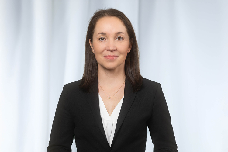Portrait einer Frau in schwarzem Anzug vor einem hellen Hintergrund.