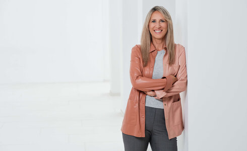 Frau mit blonden Haaren lächelt und steht an einer Wand.