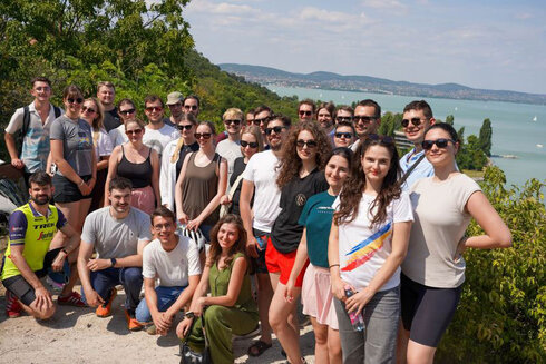 Eine Gruppe von 35 Personen posiert am Ufer eines Sees bei sonnigem Wetter.