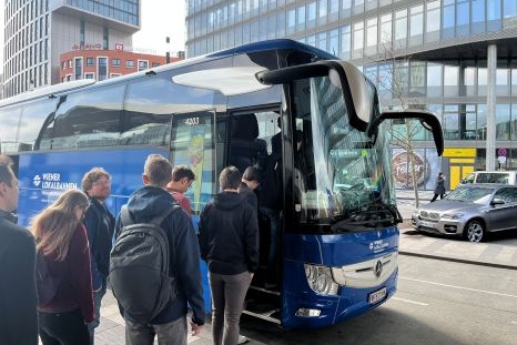 Ein Gruppen von Personen steigt in einen blauen Reisebus ein.