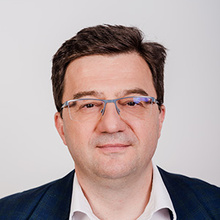 Porträt eines Mannes mit Brille, in einem Anzug mit blauem Muster.