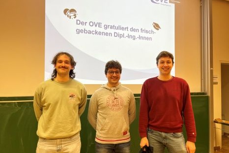 Drei Männer stehen vor einer Präsentation zur Gratulation frisch gebackener Ingenieure.