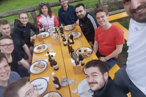 Gruppentreffen mit Essen und Getränken an einem Tisch im Freien.