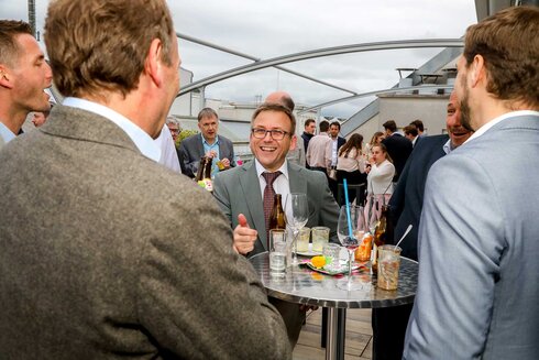 Menschen in Anzügen unterhalten sich bei einer Veranstaltung auf einer Dachterrasse.