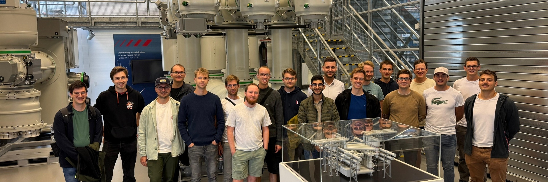 Gruppe von Personen steht vor industriellen Maschinen in einer modernen Fertigungshalle.