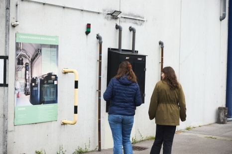 Zwei Personen stehen vor einer Wand mit einer Tür und einem Plakat.