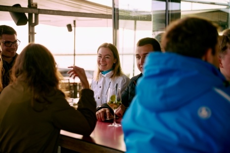 Junge Erwachsene unterhalten sich an einer Bar mit Getränken in entspannter Atmosphäre.