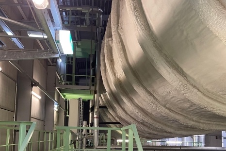 Großer, runder Behälter in einer Industriehalle, umgeben von Metallstrukturen.