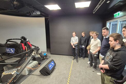 Eine Gruppe von Menschen beobachtet ein Simulator-Gerät in einem modernen Raum.