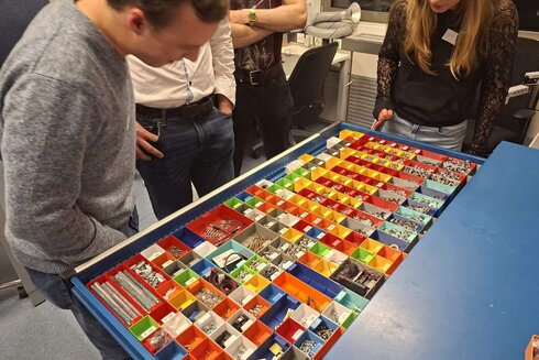 Eine Gruppe von Personen betrachtet eine Sammlung farbiger Boxen mit verschiedenen Objekten.