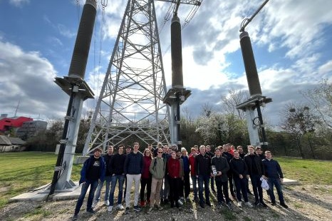 Gruppe von Menschen vor einem Hochspannungsmast an einem bewölkten Tag.