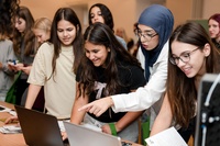 Gruppe junger Frauen, die gemeinsam an Laptops arbeiten und diskutieren.