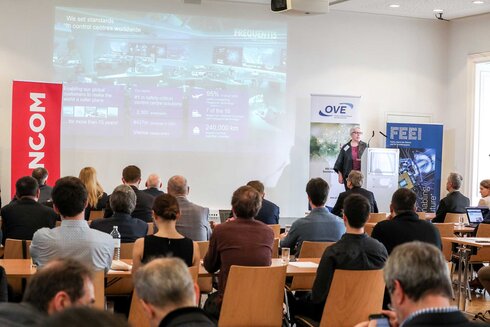 Vortrag auf einer Konferenz mit Publikumsinteraktion und Präsentation im Hintergrund.