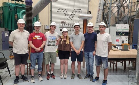 Gruppe von sieben Personen in Sicherheitshelmen in einer technischen Umgebung.