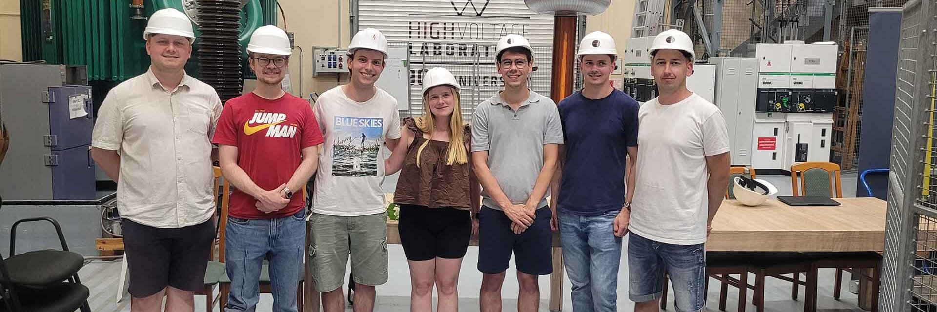 Gruppe von sieben Personen in Sicherheitshelmen in einer technischen Umgebung.