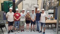 Gruppe von sieben Personen in Sicherheitshelmen in einer technischen Umgebung.