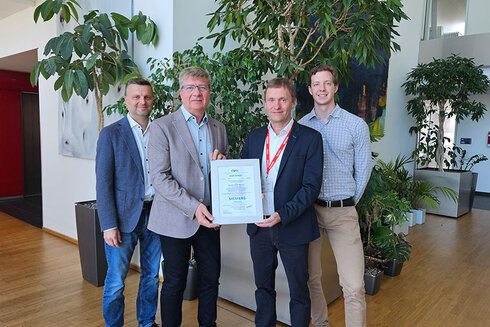 Vier Personen halten eine Urkunde in einem modernen Büroumfeld voller Pflanzen.