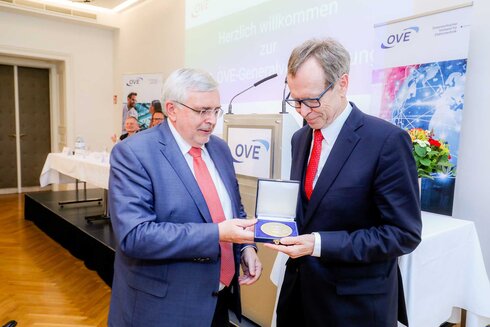 Zwei Männer überreichen eine Medaille während einer Veranstaltung.