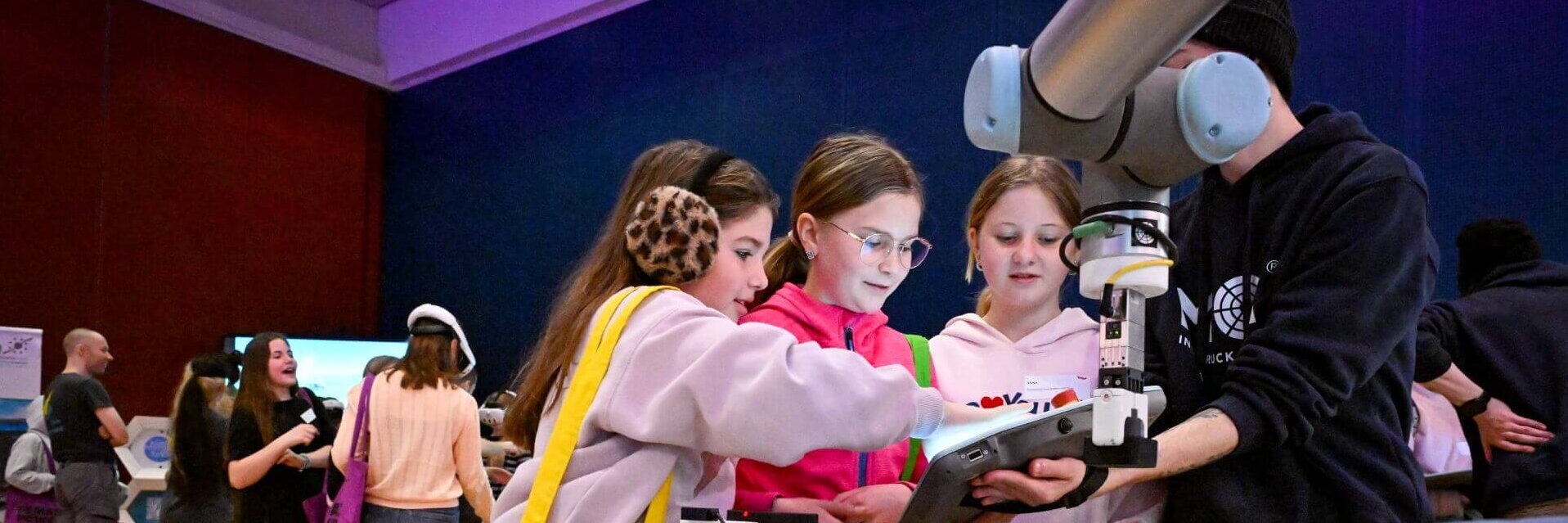 Vier Kinder interagieren mit einem Roboterarm auf einer Technikveranstaltung.