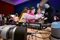 Vier Kinder interagieren mit einem Roboterarm auf einer Technikveranstaltung.