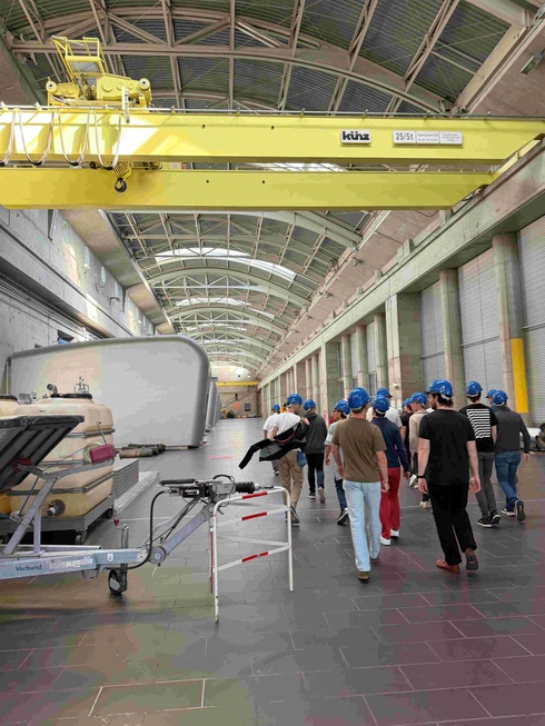 Gruppen von Personen mit Helmen gehen in einer großen Industriehalle.