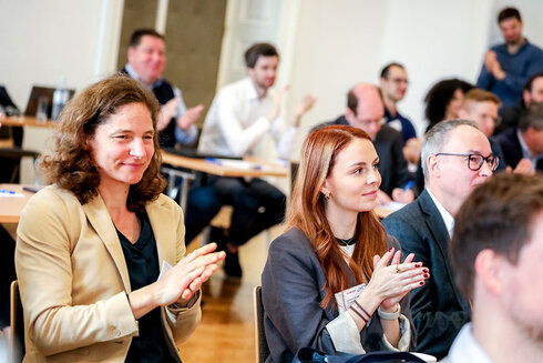 Zuhörer applaudieren während einer Veranstaltung, einige lächeln zufrieden.
