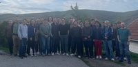 Eine Gruppe von etwa 30 Menschen steht lächelnd im Freien vor einer Landschaft.