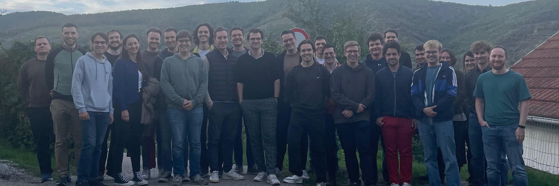 Eine Gruppe von etwa 30 Menschen steht lächelnd im Freien vor einer Landschaft.