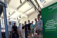 Eine Gruppe von Menschen steht vor einem Werbebanner von Kärnten Netz.