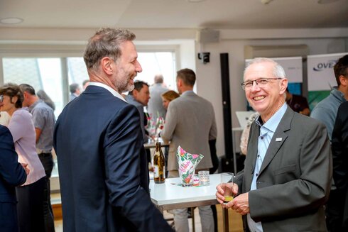 Zwei Männer unterhalten sich bei einer Veranstaltung in einem modernen Raum.