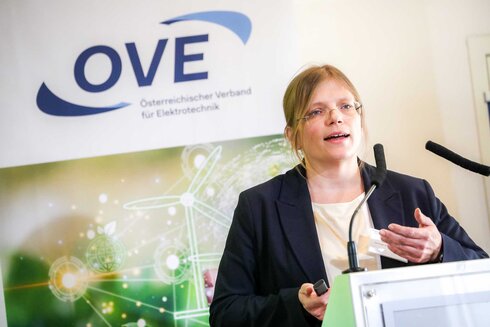 Eine Frau hält einen Vortrag vor einem OVE-Logo.