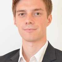 Porträt eines jungen Mannes in Anzug mit neutralem Gesichtsausdruck.