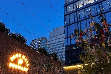 Restaurant mit leuchtendem Schild und modernen Gebäuden im Hintergrund bei Dämmerung.