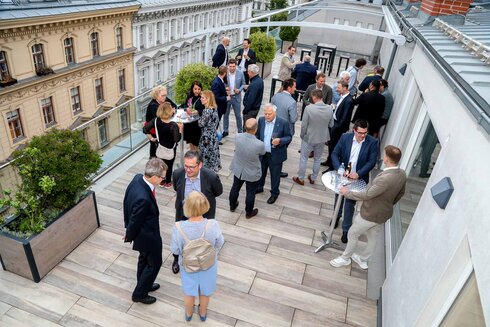 Menschen stehen auf einer Dachterrasse und unterhalten sich bei einem Event.