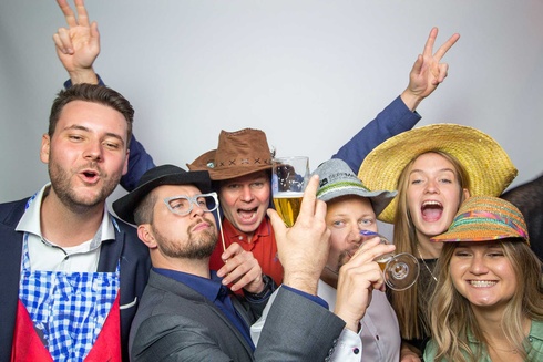 Gruppenselfie mit sechs Personen in bunten Hüten, die feiern und anstoßen.