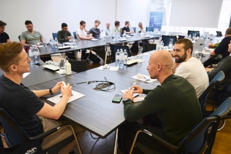 Gruppendiskussion an einem Tisch mit mehreren Personen und Getränken.