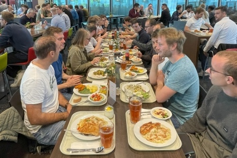 Menschen sitzen an einem langen Tisch und genießen gemeinsam ihr Mittagessen.