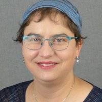 Porträt einer lächelnden Frau mit Brille und Kopfbedeckung.