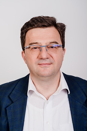 Porträt eines Mannes mit Brille, in einem Anzug mit blauem Muster.