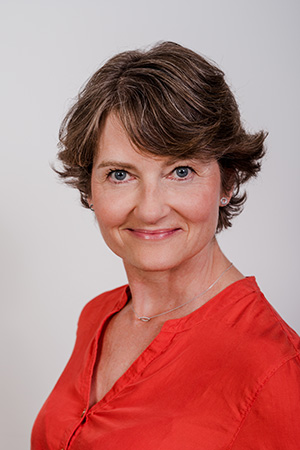 Porträt einer lächelnden Frau mit kurzen, braunen Haaren in rotem Oberteil.