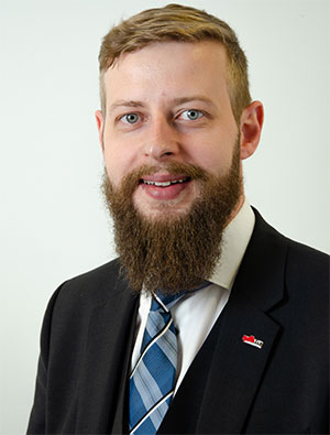 Porträt eines Mannes mit Bart in formeller Kleidung und Krawatte.