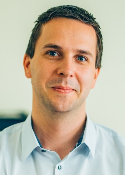 Portrait eines lächelnden Mannes mit blauen Augen und leichtem Bart.