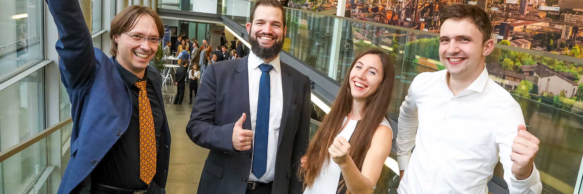 Vier Menschen lächeln und zeigen Daumen hoch in einem modernen Umfeld.